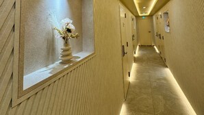 A long, narrow hallway with a beige color scheme, featuring a decorative alcove with a vase of flowers and a textured wall. - song stay (Dangjin)