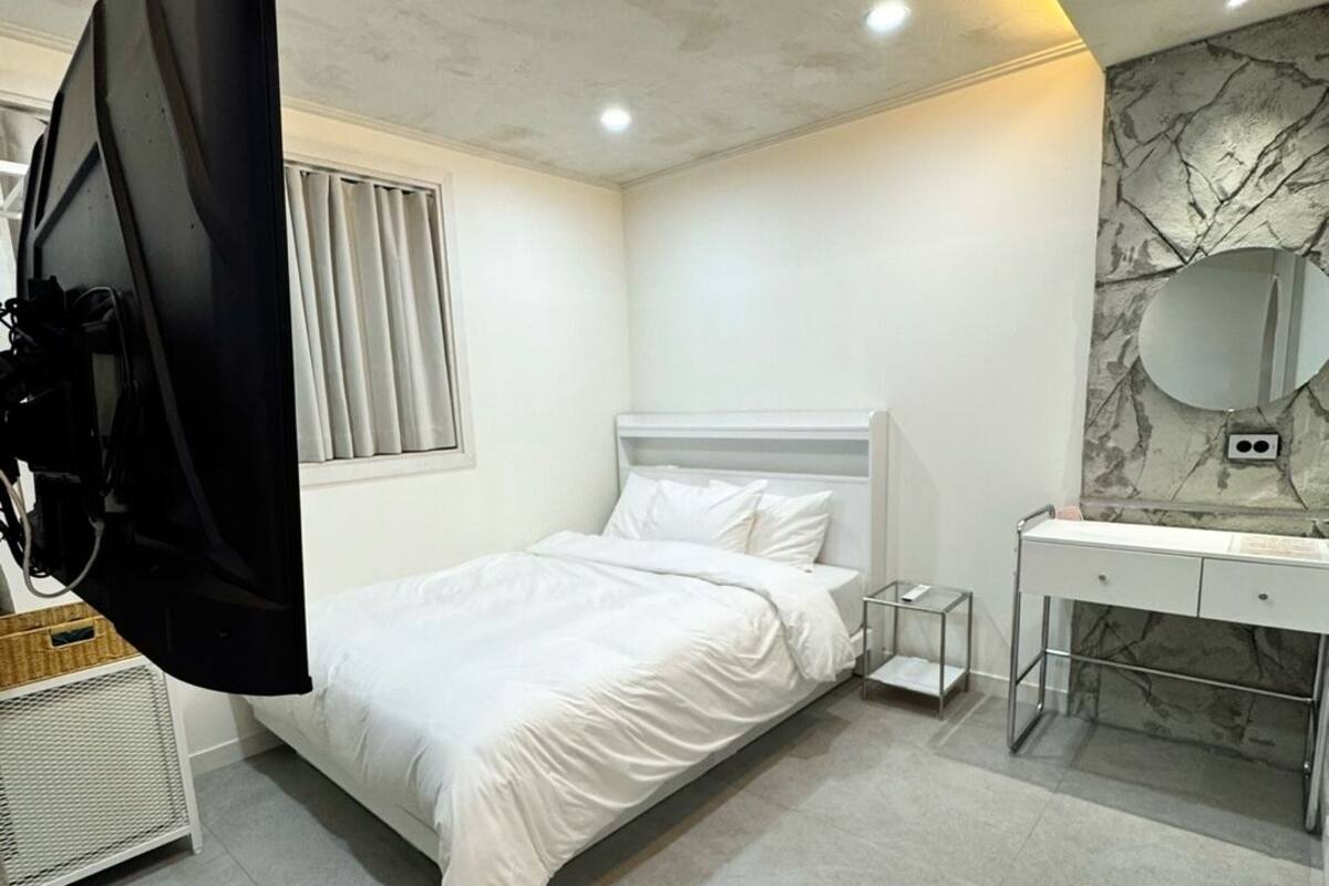 A modern bedroom with a bed, a desk, a mirror, and a television.