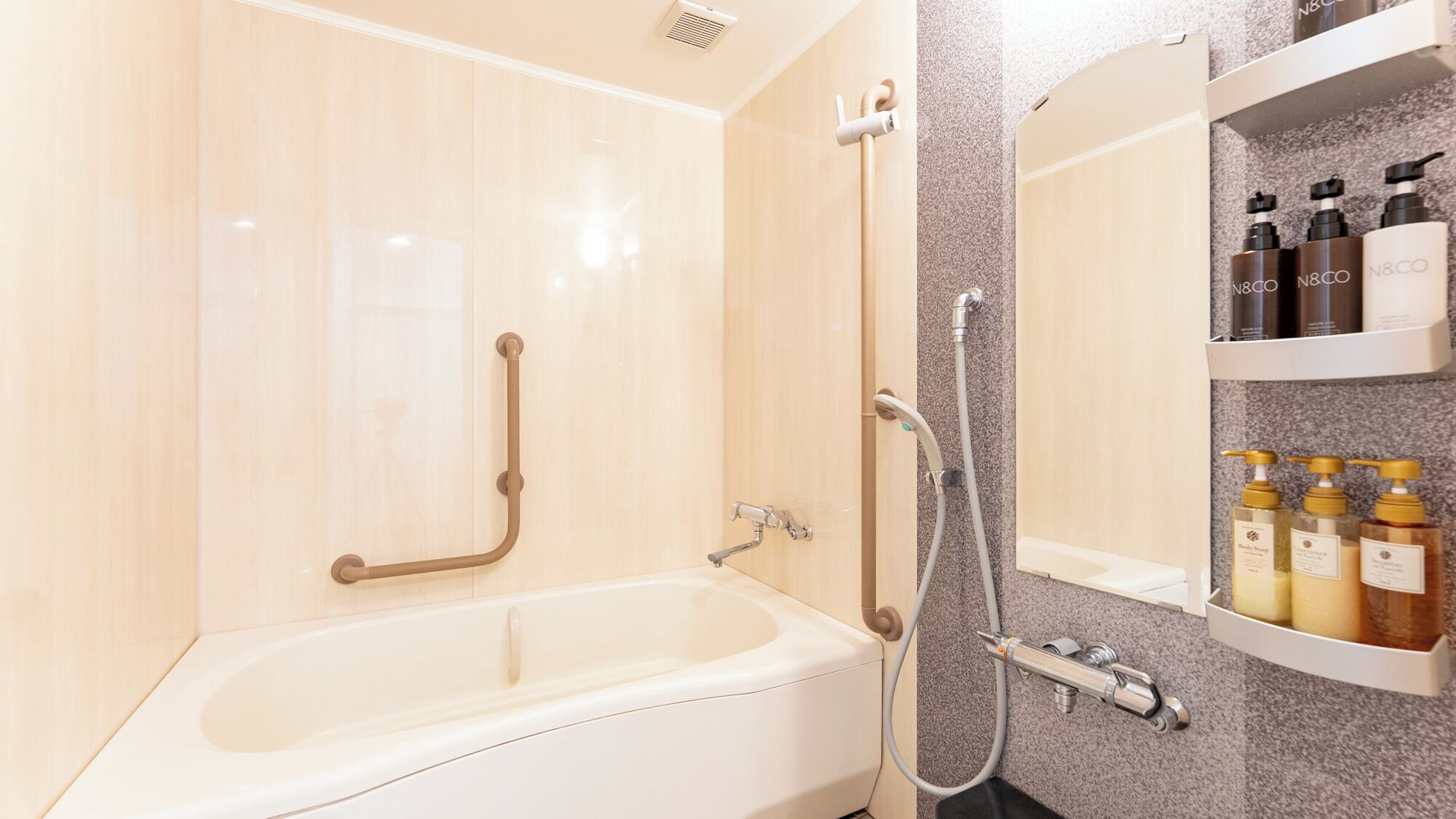 A modern bathroom with a bathtub, grab bars, a shower, and a shelf with toiletries.