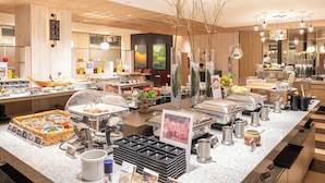 Zona de bufé con diversas estaciones de comida, que incluye una barra de ensaladas y un mostrador con opciones de café y té.