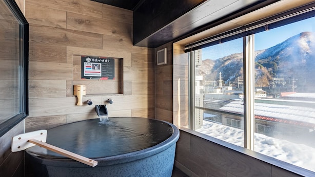 Un baño de aguas termales con paredes de madera y una ventana con vista a un paisaje nevado.