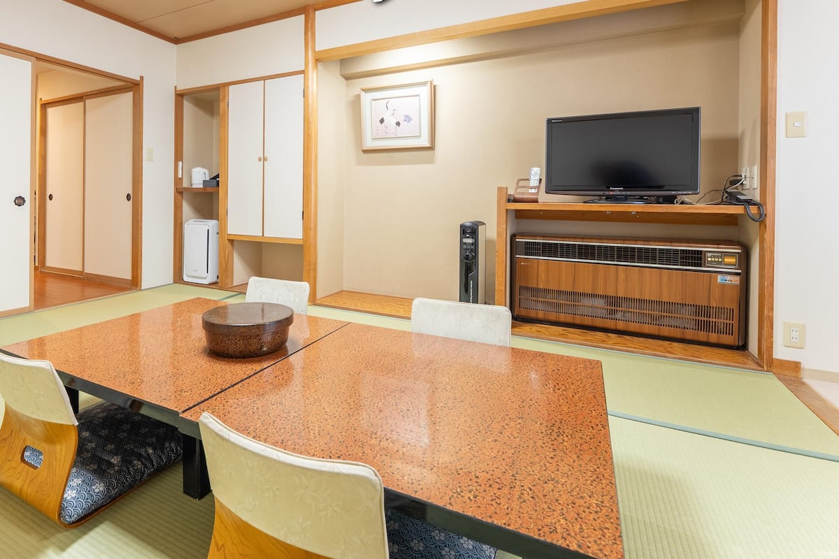 A traditional Japanese-style room with tatami flooring, a low table with a bowl, and a television on a wooden stand.