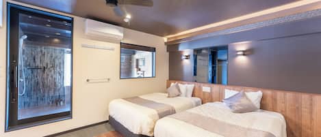 A hotel room with two beds, a ceiling fan, a large window, and a shower area.
