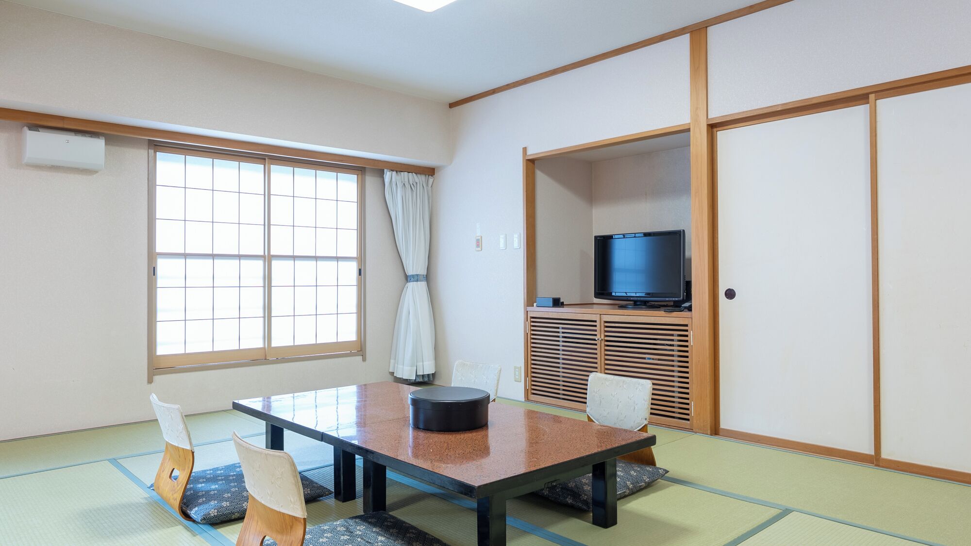 A traditional Japanese room with tatami flooring, a low table, two chairs, a television, and sliding doors.