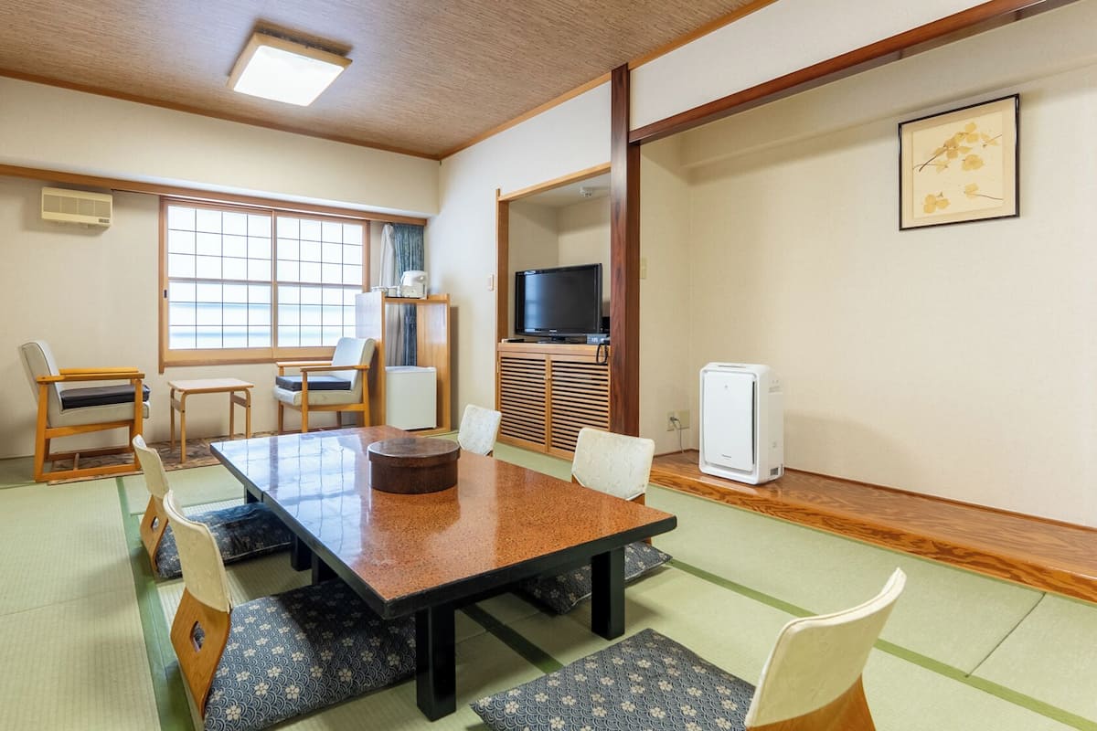 A traditional Japanese-style room with tatami flooring, a low table with cushions, a television, and a small refrigerator.