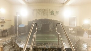 Un onsen japonés tradicional con escalones de piedra que conducen a una fuente termal, paredes de piedra y un banco de madera.