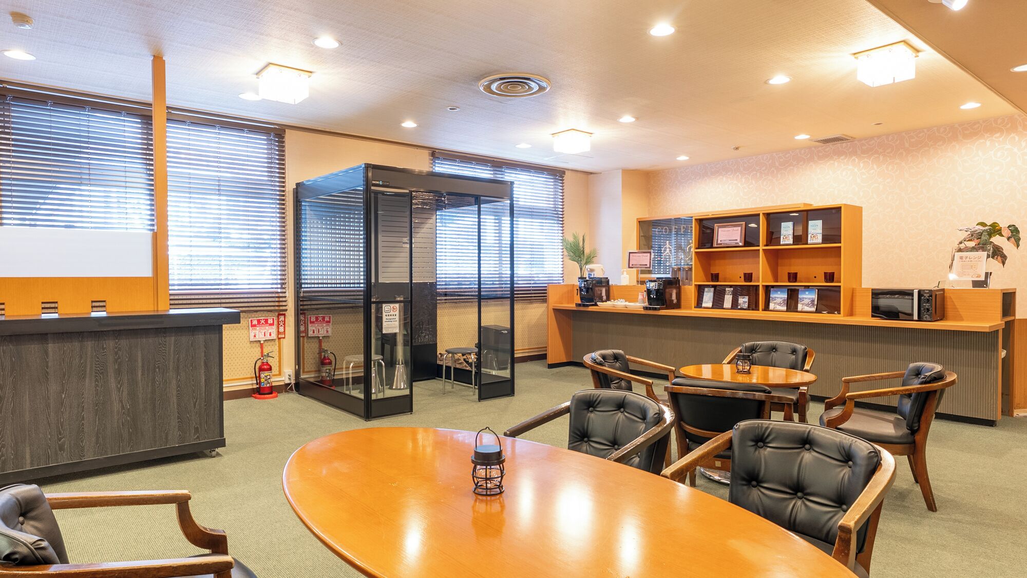 Een vergaderzaal met een houten tafel, lederen stoelen, een glazen scheidingswand en een receptiebalie met een koffieapparaat.