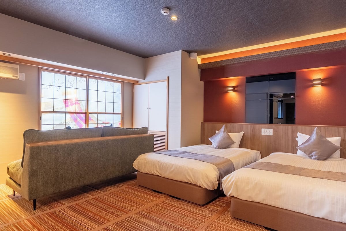 A hotel room with two beds, a sofa, a large window, and a mirror.