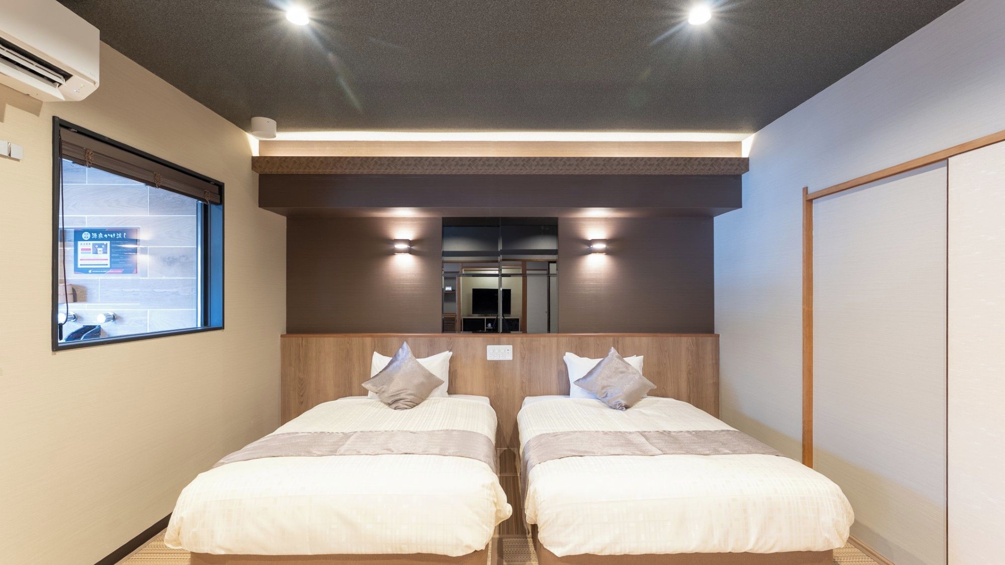 Une chambre d’hôtel avec deux lits, une fenêtre et un miroir.