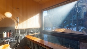 Una sauna con un banco de piedra, pared de madera y ventana con vista a un paisaje nevado.