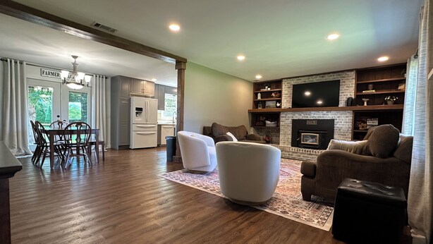 A spacious living room with a fireplace, a dining area with a table and chairs, and a kitchen with a refrigerator and cabinets.