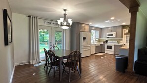 A spacious kitchen with wooden flooring, a dining table with chairs, and a view of the outdoors through a glass door.