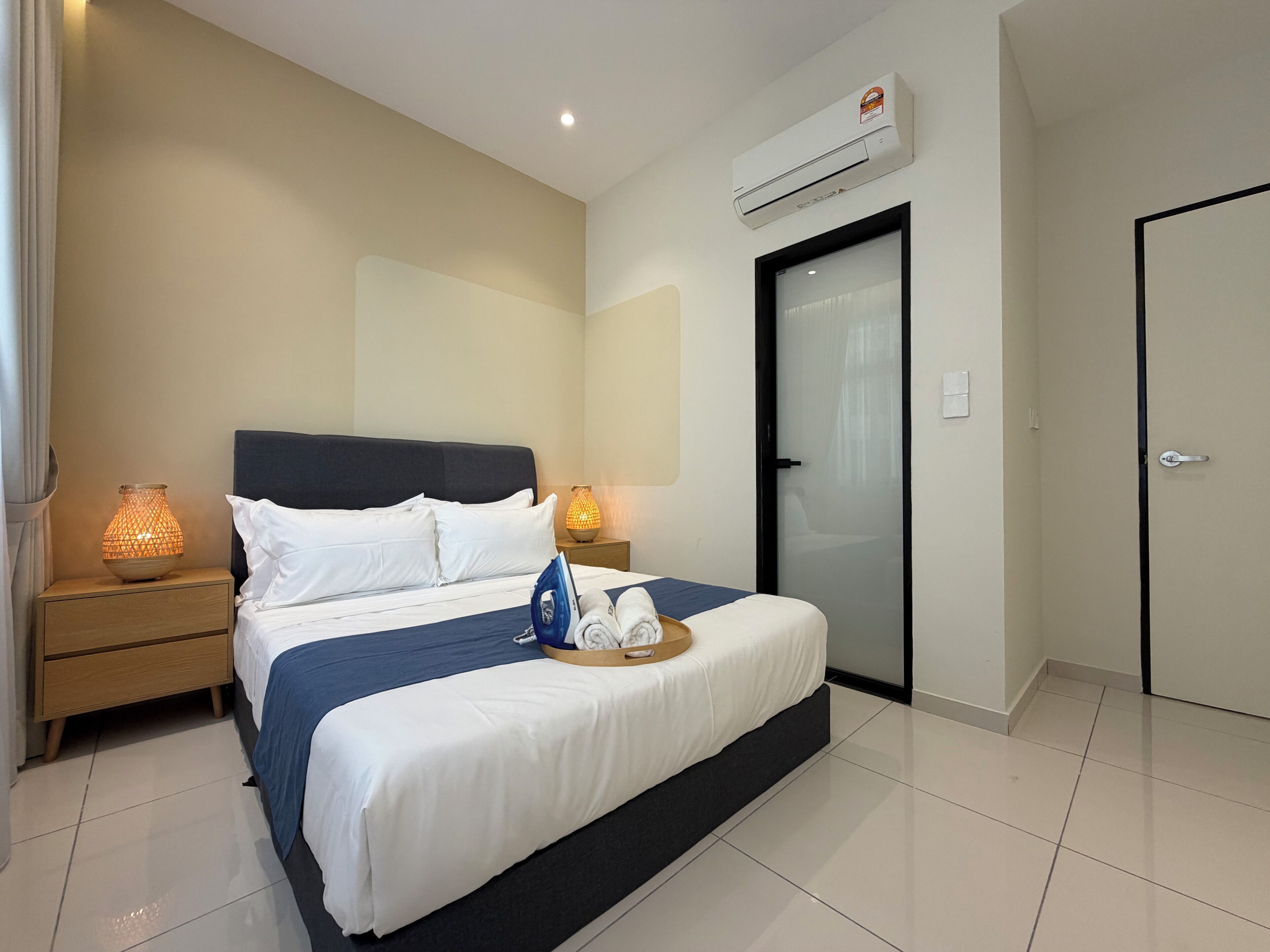 A hotel room with a bed, bedside lamps, an air conditioner, a door, and a tiled floor.