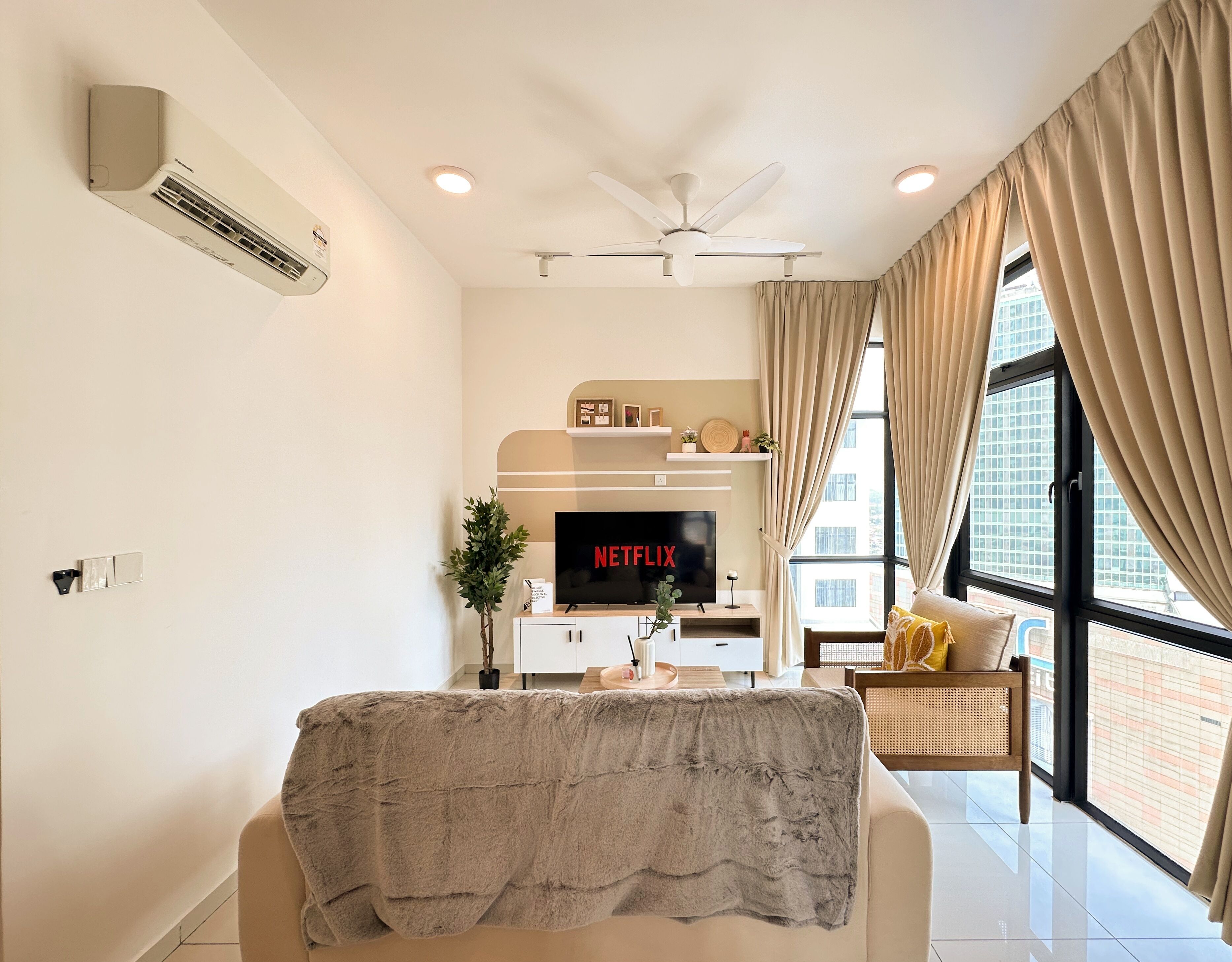 Ein modernes Wohnzimmer mit Flachbildfernseher, Deckenventilator und großen Fenstern mit Vorhängen.