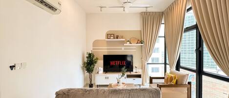 Ein modernes Wohnzimmer mit Flachbildfernseher, Deckenventilator und großen Fenstern mit Vorhängen.
