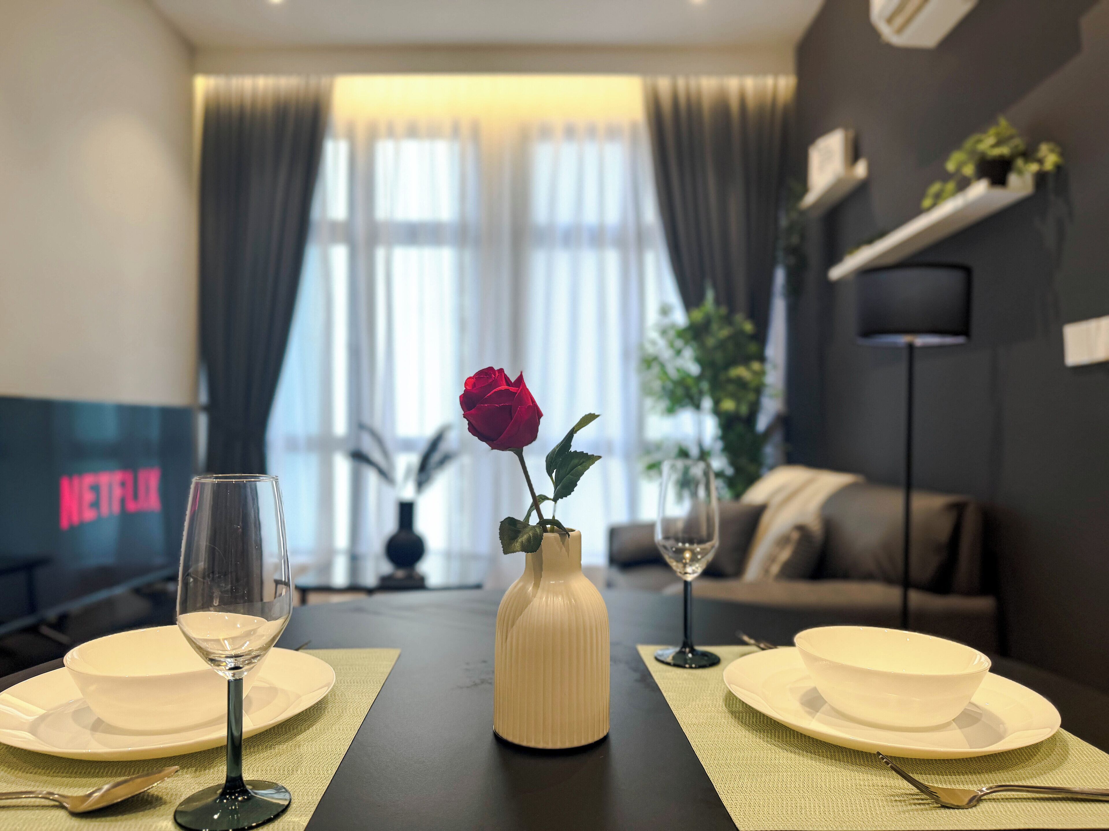 A dining table with a vase of a red rose, two wine glasses, and a Netflix sign in the background.