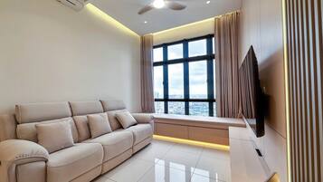 Un salon moderne avec un canapé, un téléviseur à écran plat fixé au mur et une grande fenêtre avec des rideaux.