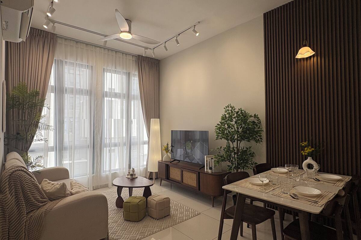 Un salon moderne comprenant un canapé, une table à manger pour quatre personnes, un téléviseur et une grande fenêtre avec des rideaux.