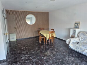 A dining area with a round mirror, wooden panel wall, and a sofa with patterned upholstery.