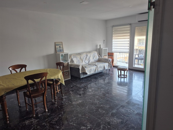 A room with a dining table, chairs, a sofa, a cabinet, and a view through a glass door.