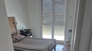 Une chambre à coucher avec un lit, un bureau, une chaise et une fenêtre avec des stores.