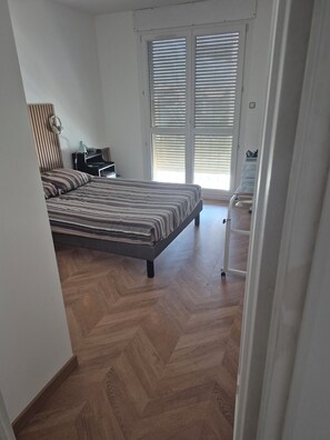 A bedroom with a bed, a desk, a chair, and a window with blinds.
