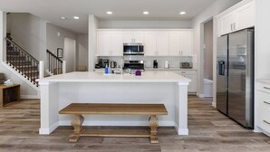 A modern kitchen with white cabinetry, a central island, stainless steel appliances, and a wooden bench. - Perch - Modern End-Unit Surrounded by Nature (Oak Harbor)