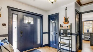 A room with a dark blue door, a guitar hanging on the wall, and a shelf with various items.