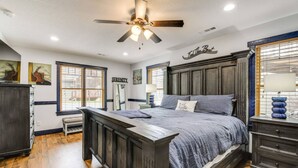 A bedroom with a large bed, a ceiling fan, and a window with blinds.