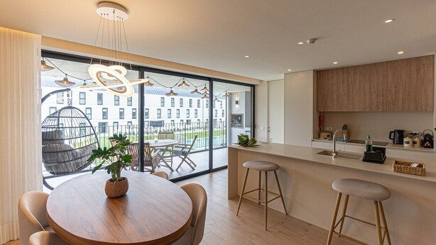 A modern kitchen with a large window, wooden furniture, and a hanging light fixture. - GuestReady - Elegant beachside stay in Apúlia (Apúlia e Fão)