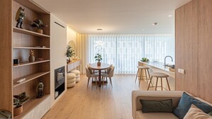 A modern living room with a wooden floor, a round dining table with chairs, a sofa with cushions, and a kitchen area with a sink and counter. - GuestReady - Elegant beachside stay in Apúlia (Apúlia e Fão)