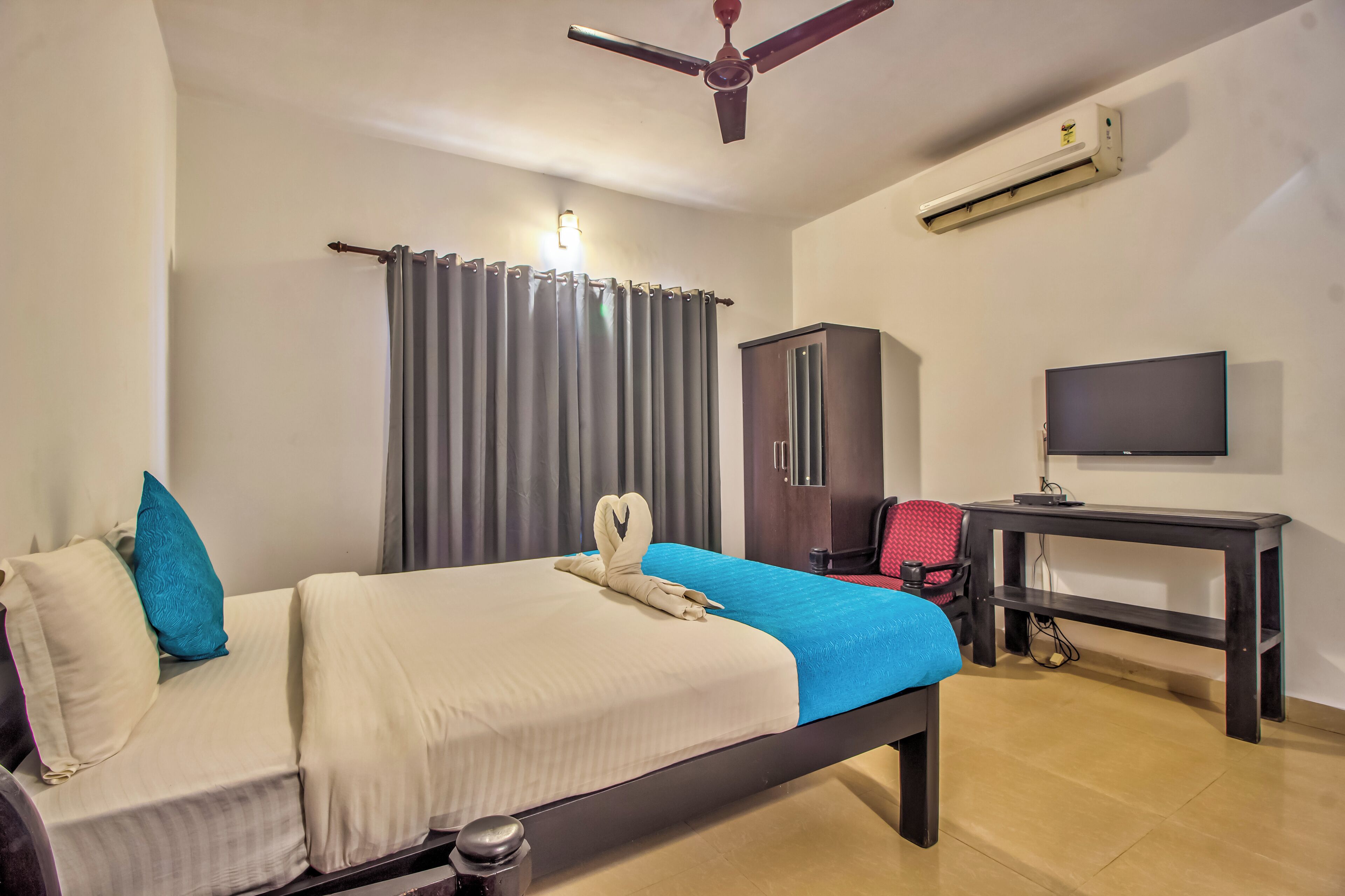 A hotel room with a bed, a desk, a television, a wardrobe, and a ceiling fan.