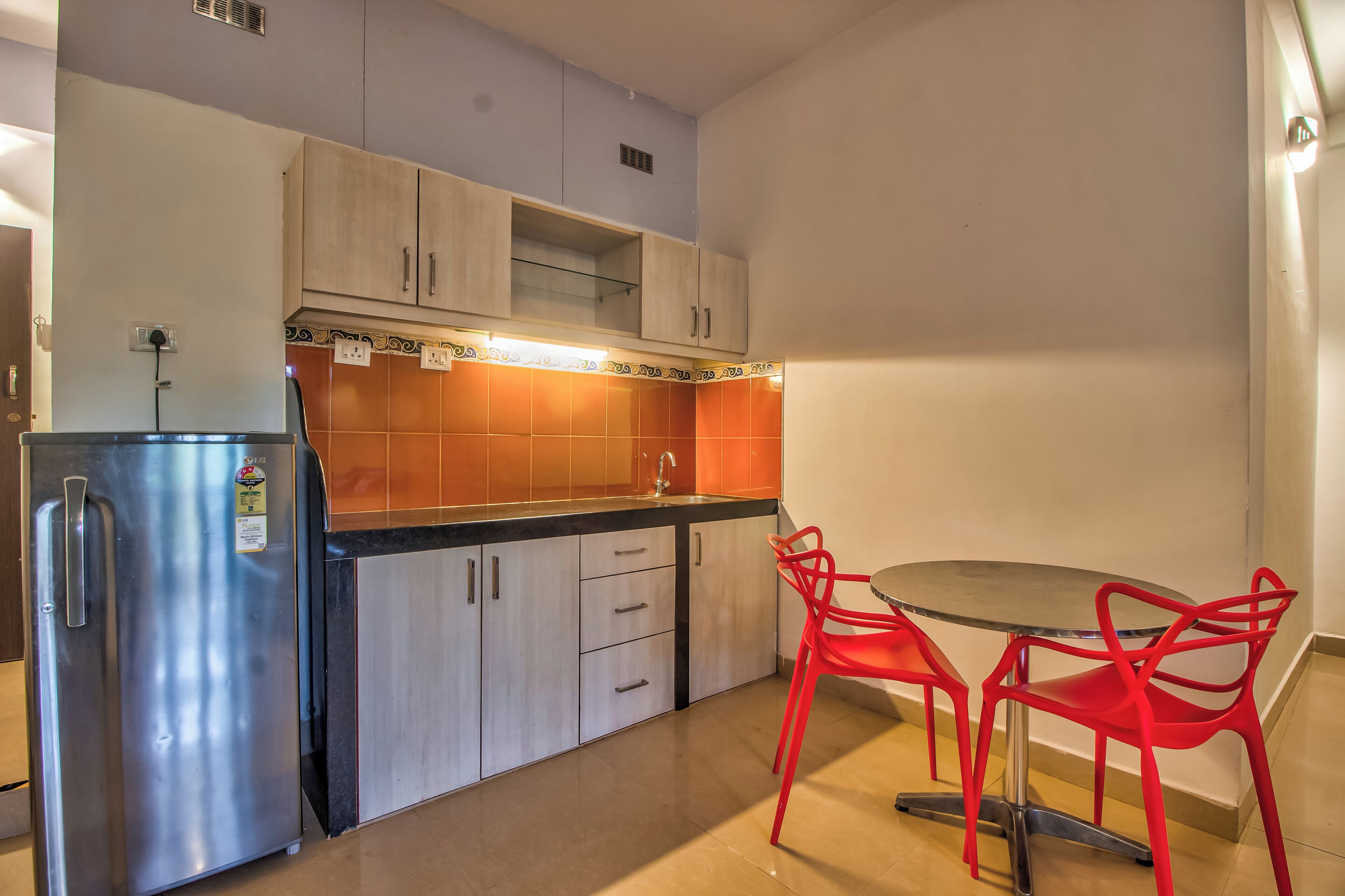 A compact kitchen with a refrigerator, cabinets, a sink, and a dining table with red chairs.