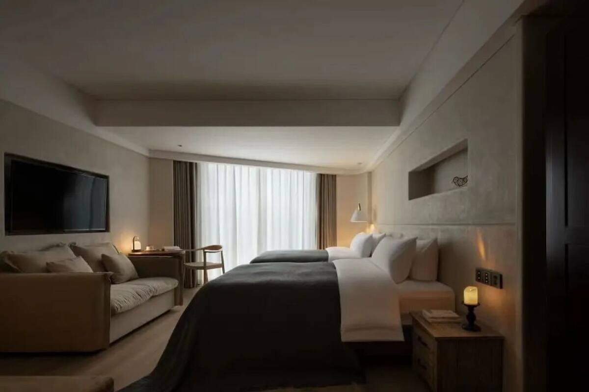 A modern hotel room with a large bed, a sofa, a TV, and a desk with a lamp.