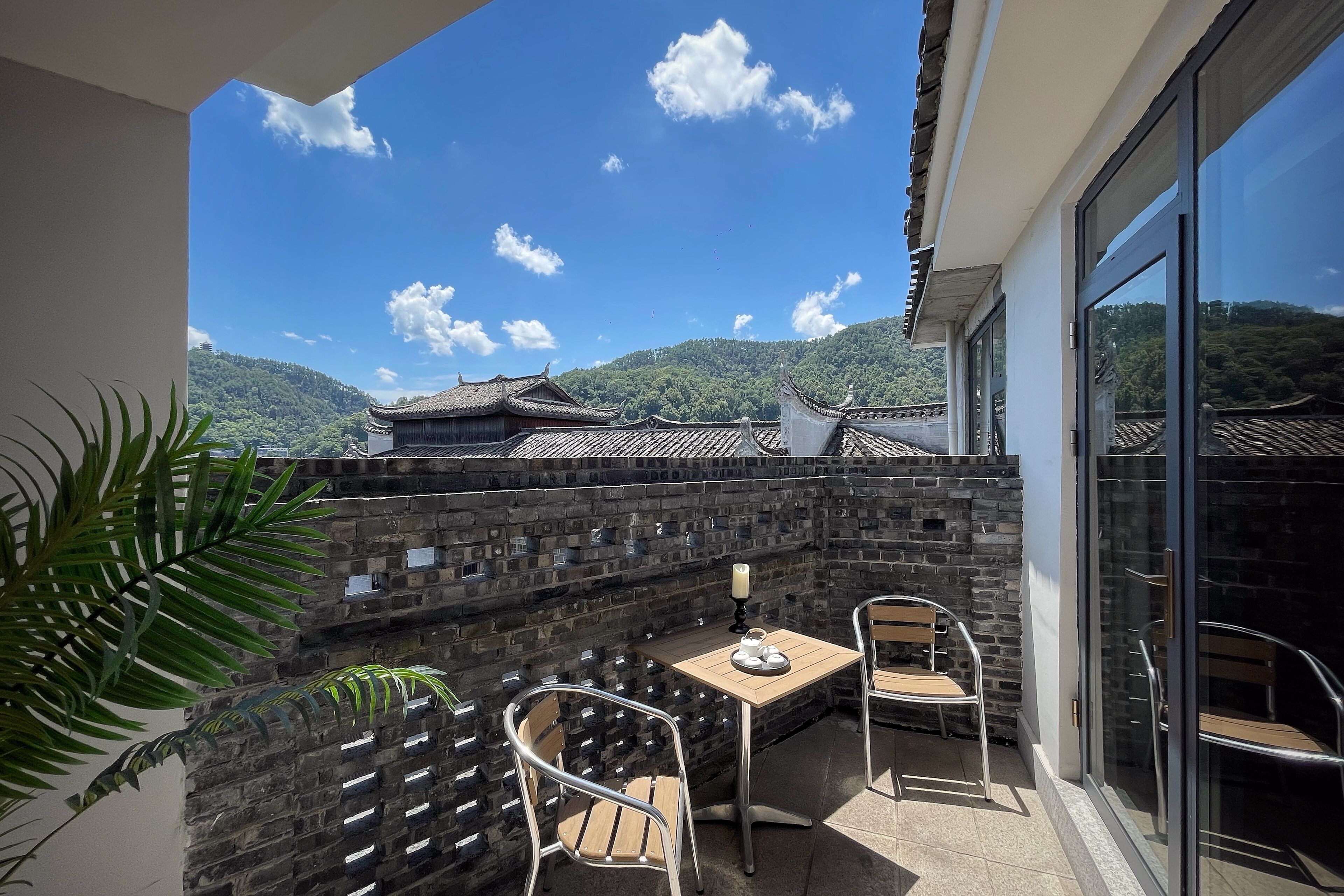 A balcony with a table and chairs, a potted plant, and a view of traditional buildings and mountains.