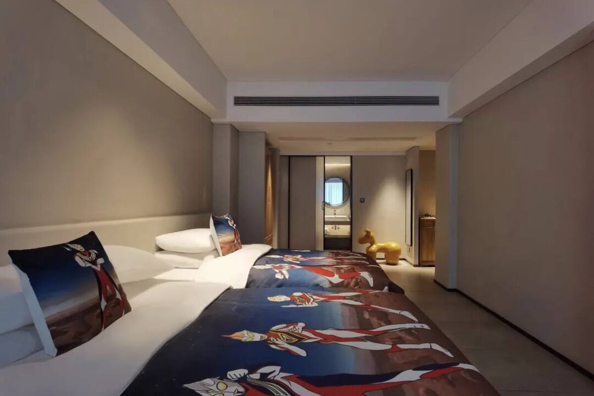 A hotel room with a large bed, a sofa, and a small table. There is a hallway leading to another room.