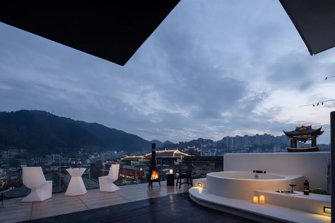 A rooftop terrace with modern seating, a fire pit, and a view of a cityscape and mountains.