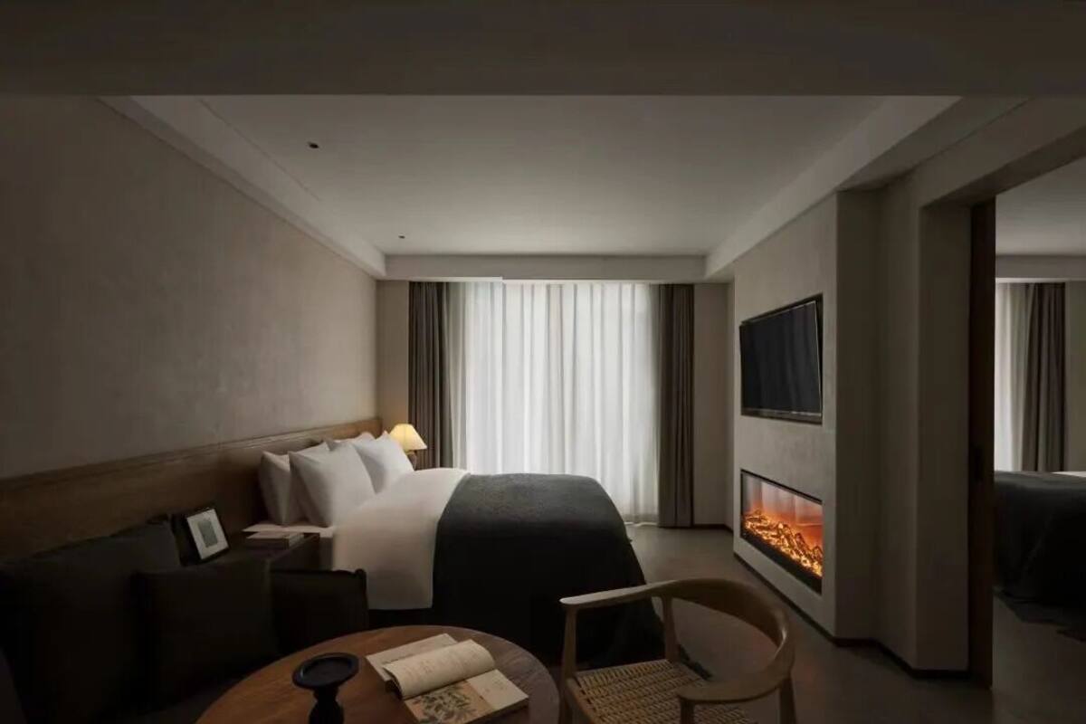 A hotel room with a bed, a TV, a fireplace, a sofa, and a dining table.