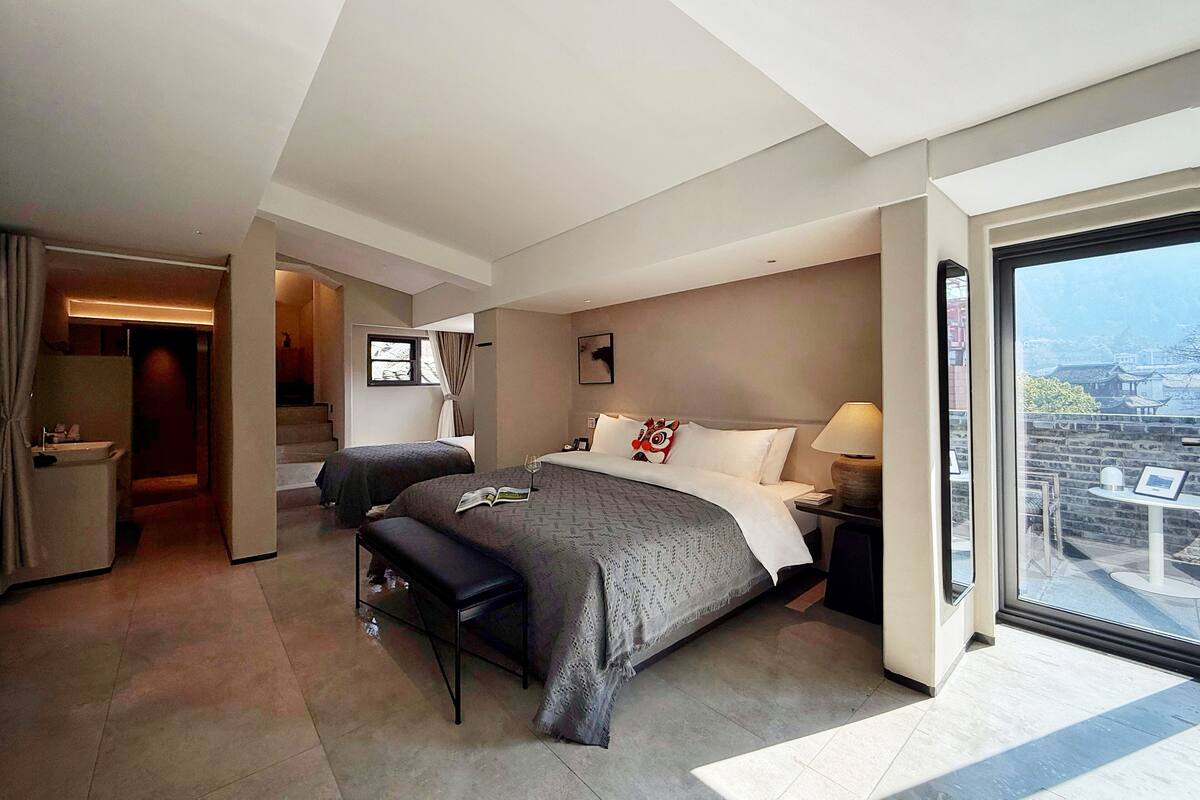 A modern hotel room with a large bed, a desk, and a balcony with a city view.