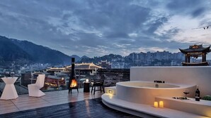 A rooftop terrace with a fire pit, seating area, and a view of a cityscape and traditional architecture. - Phoenix Hall House Hotel (Xiangxi)