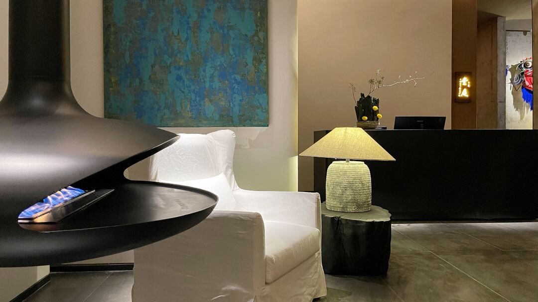 A modern hotel lobby with a white sofa, a black table with a remote control, a lamp, and a large abstract painting on the wall.