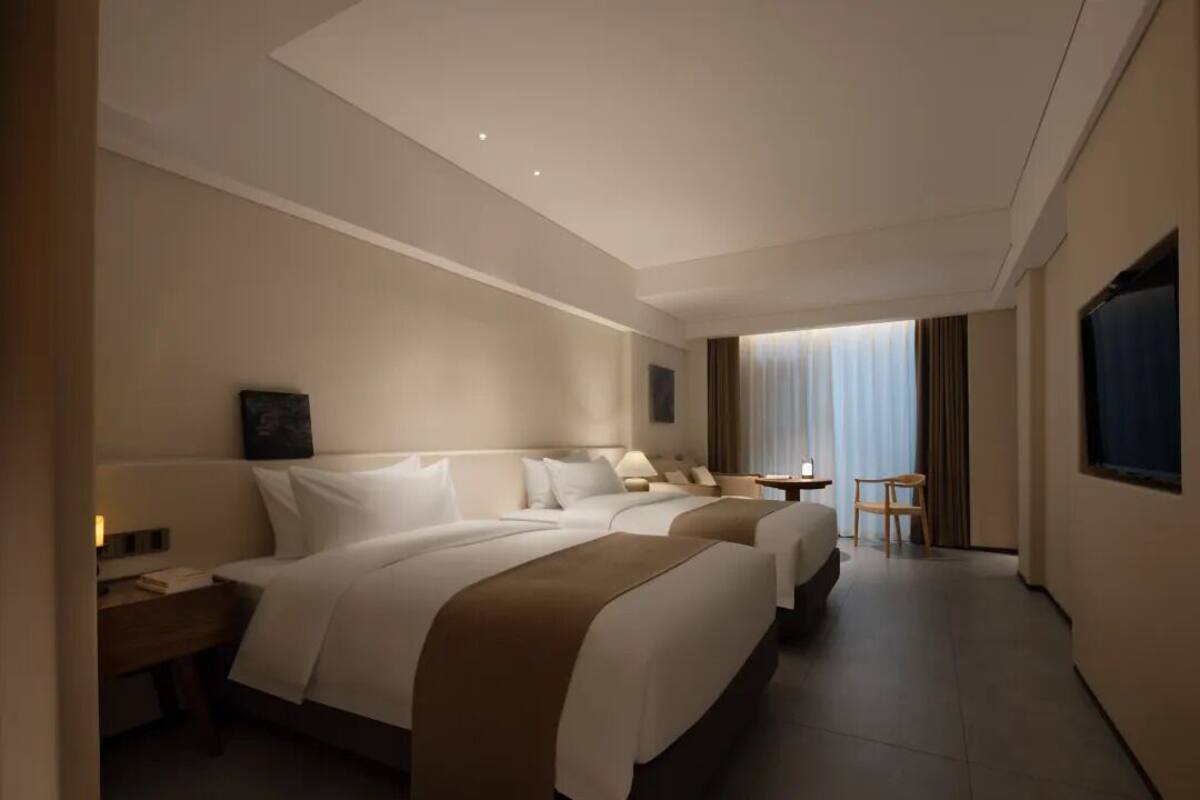 A hotel room with two beds, a small table, a chair, and a TV.