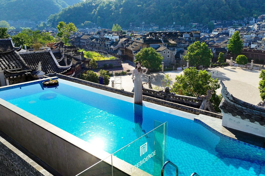 A swimming pool with a traditional architectural backdrop, a clear sky, and a distant town view.