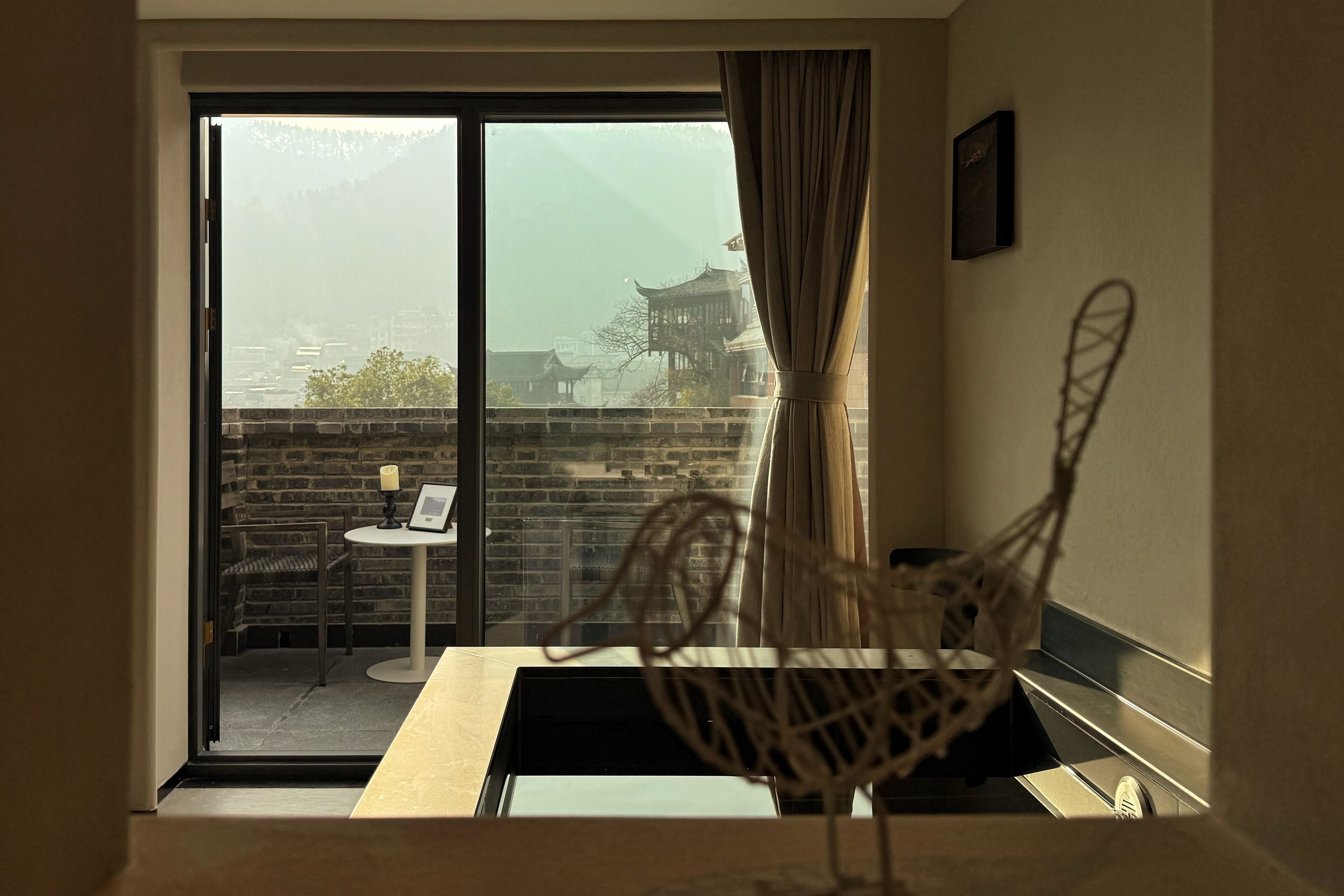 A room with a sliding glass door leading to a balcony with a view of traditional architecture and a table with chairs.