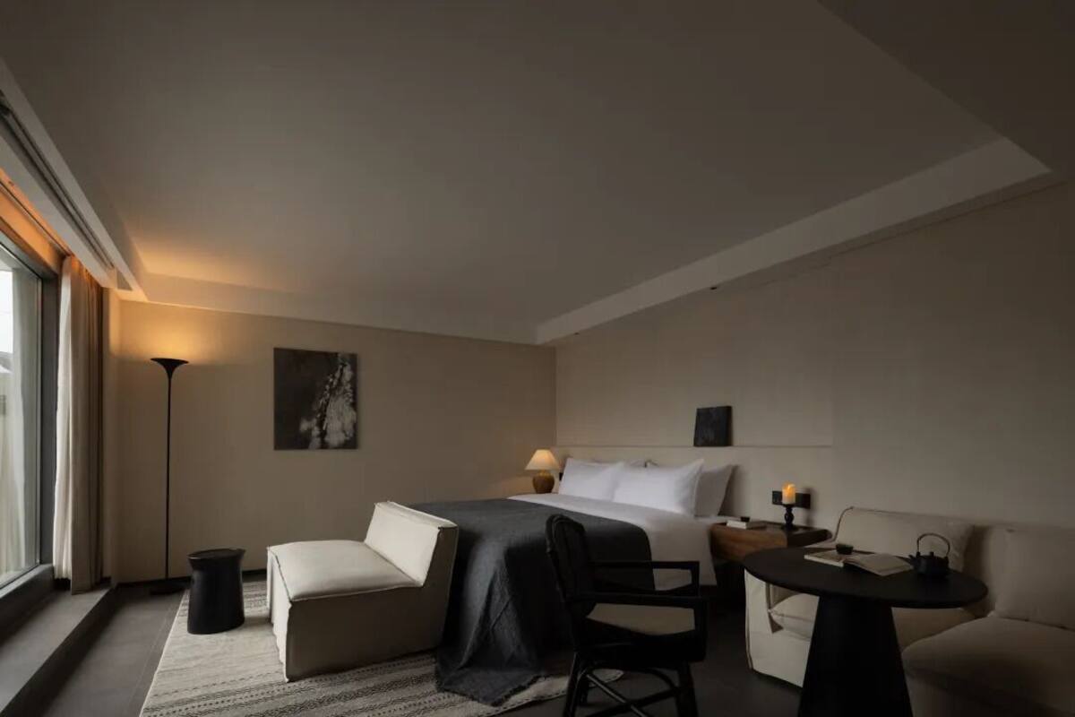 A modern hotel room with a bed, a desk, a chair, a small table, and a sofa.