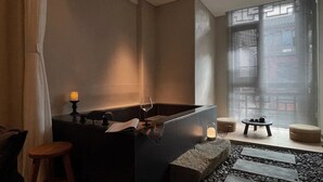 A modern bathroom with a large bathtub, a small stool, and a table with candles. - Phoenix Hall House Hotel (Xiangxi)