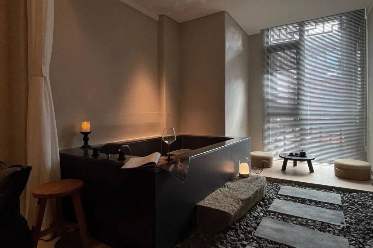 A modern bathroom with a large bathtub, a small stool, and a table with candles.