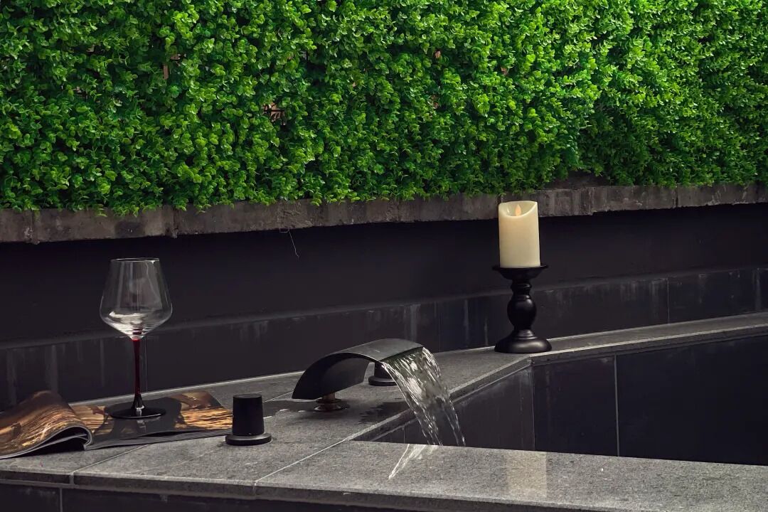 A modern bathroom with a green wall, a glass of red wine, a candle, and a water feature.