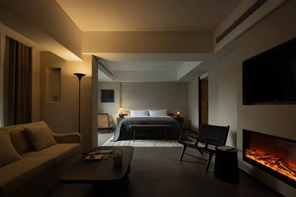 A modern hotel room with a sofa, a coffee table, a fireplace, a bed, and a TV mounted on the wall.