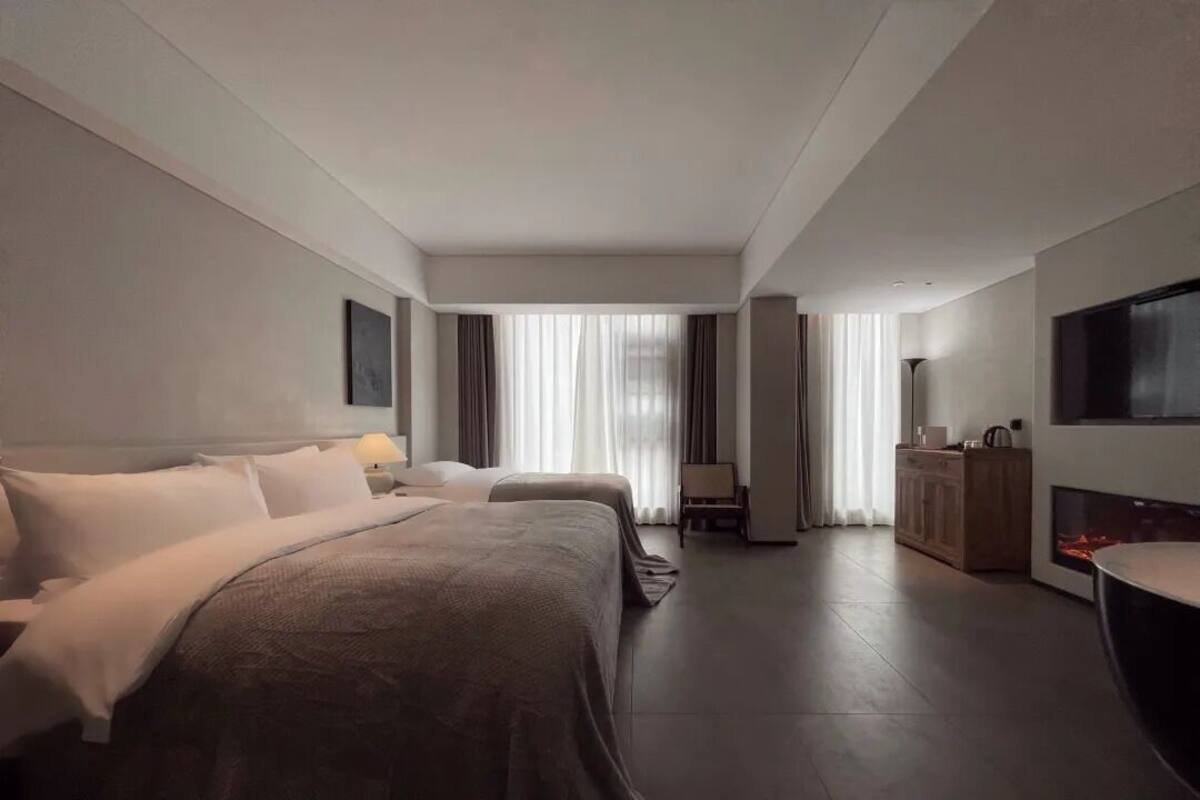 A hotel room with two beds, a flat-screen TV, a desk, and a fireplace.
